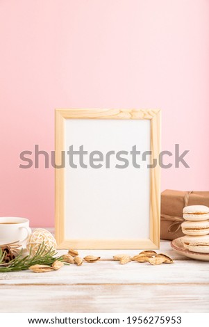 White wooden frame mockup with cup of coffee, almonds and macaroons on pink pastel background. Blank, side view, still life.
