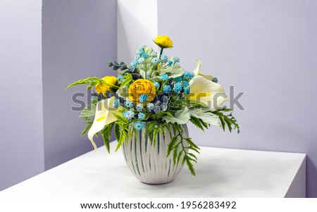 bouquet of yellow, white and blue flowers in a small round vase on a light background, side view. Copy space. Flowers for the interior. Artificial bouquet Royalty-Free Stock Photo #1956283492