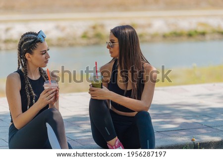 Two girls sit in a park while taking a break from rollerskating drinking smoothie and gossiping. Girls bonding concept.