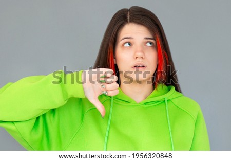 Young woman showing her disliking of something with her thumb down, isolated against gray background