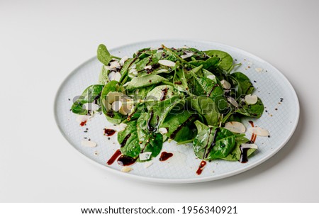 Spinach salad on white, with beetroot, arugula, balsamic vinegar, black sesame seeds, almond petals and feta cheese over light grey slate. Top view.