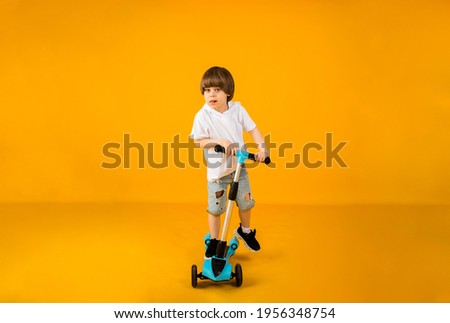 happy little boy riding a scooter on a yellow background with space for text