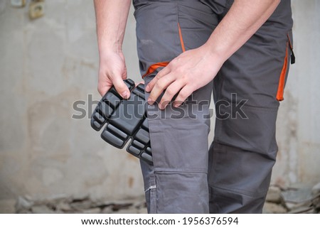 Unrecognizable builder wearing knee protection pads to work in a construction. Safety at work. Royalty-Free Stock Photo #1956376594