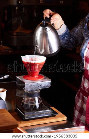 Girl barista brews coffee in red v60 pourover. Dripping water from funnel in hand into a server on electronic scale Royalty-Free Stock Photo #1956383005