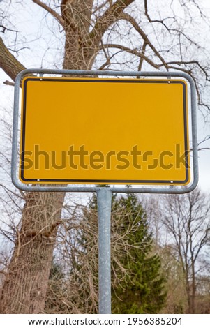 Yellow sign without content in front of a tree in winter.