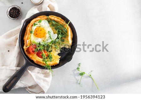 Dutch baby pancake with egg, greens and tomatoes in a cast-iron pan on a white table, top view, sunlight,  breakfast Royalty-Free Stock Photo #1956394123