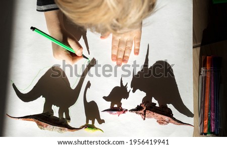 child, with enthusiasm and concentration, outlines shadows from toy figurine of small and large dinosaurs. development of fine motor skills. children's entertainment. Ideas for creativity for kid