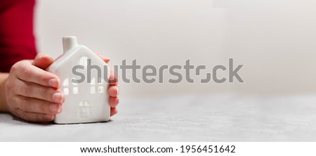 Female hands hold a small cozy house on a gray background with copyspace