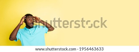 Surprised. Young African man isolated on yellow studio background with copyspace for ad. Male fashion model in blue shirt. Concept of human emotions, facial expression, youth. Trendy colors. Flyer
