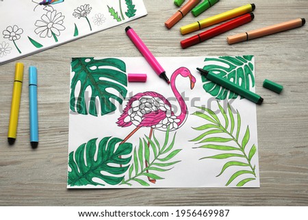 Coloring pages with children drawings and set of felt tip pens on wooden table, flat lay