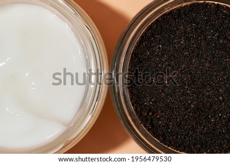 Facial scrub and cosmetological cream in open round cans on light orange background, flat lay, top view. Beauty treatment products concept