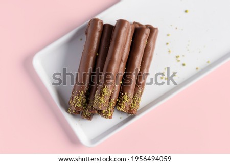 Dark Chocolate with chocolate and pistachio nuts in the top on pink background 
