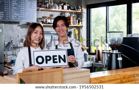 Two barista or coffee maker man and woman hold banner of open for the symbol of ready to service for customer in coffee shop. Concept of happy working with small business and sustainable.