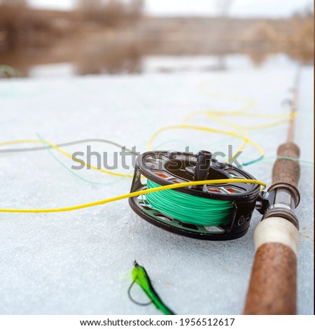 winter fly fishing picture. Fly rod and reel on snowy river bank.