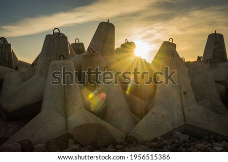 sunset with sunbeams on the background of large boulders on the sea pier