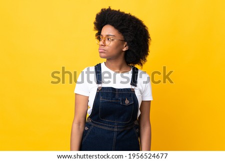 Young African American woman isolated on yellow background looking to the side