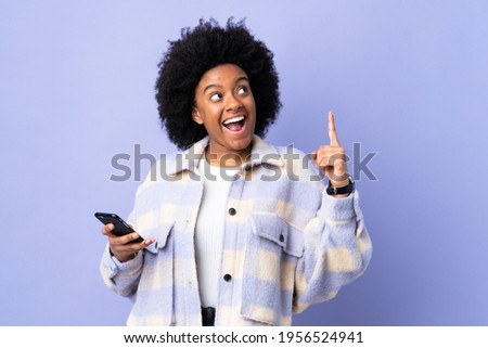 Young African American woman using mobile phone isolated on purple background intending to realizes the solution while lifting a finger up