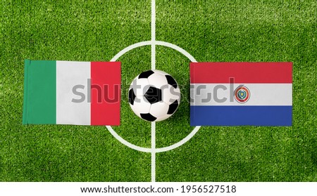 Top view ball with Italy vs. Paraguay flags match on green football field.