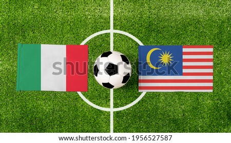 Top view ball with Italy vs. Malaysia flags match on green football field.
