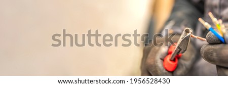 Electrician cuts electrical wires with pliers, installation of household electrical appliances, electrician tools. Panoramic photo Royalty-Free Stock Photo #1956528430