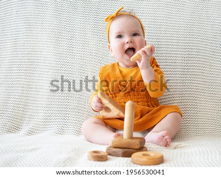 little baby girl plays with wooden rainbow toy pyramid sitting on couch