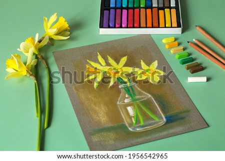 Soft pastel painting at home. Daffodils in soft pastel. Set of colored pastels, fresh daffodils and pastel picture on the mint background. Top view