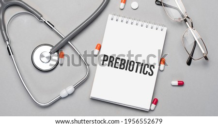 In the notebook is the text PREBIOTICS, next to a stethoscope, pills and glasses.