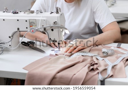 Woman sews behind sewing machine at work Royalty-Free Stock Photo #1956559054