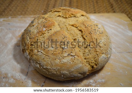 Freshly baked healthy homemade bread on a wooden baking board; crispy crust of bread with poppy seeds and linseed
