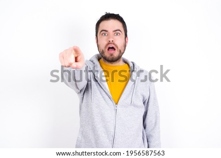 Young caucasian man wearing tracksuit over white background Pointing with finger surprised ahead, open mouth amazed expression, something on the front.