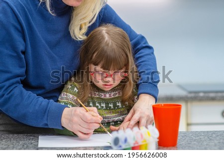 A girl with down syndrome sits next to her mother and is engaged in creativity, drawing a picture in an album. Education for people with disabilities concept.