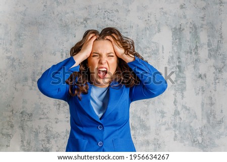 Furious  woman screaming and holding her head. Emotional  lady shouting in anger, being aggressive or mad, suffering from stress. headache. The young woman is angry and screaming, holding her head. Royalty-Free Stock Photo #1956634267