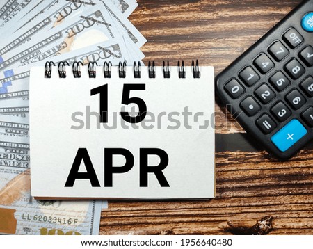 Tax concept.Text 15 APR with banknote and blur calculator on a brown wooden background.
