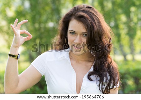 Beautiful girl on nature shows a sign "OK"