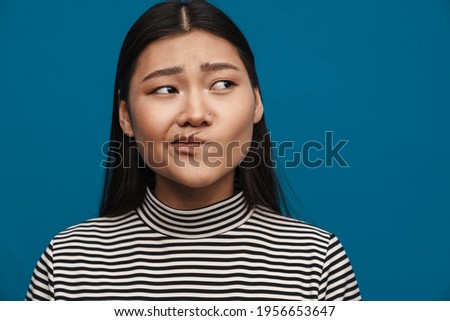 Displeased asian teen girl posing and looking aside isolated over blue background