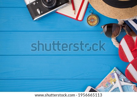 Overhead photo of camera notebook pencil compass hat sunglasses sandals map and airplane isolated on the blue background with empty space
