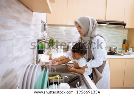 beautiful muslim mother wash her son hand in the kitchen sink