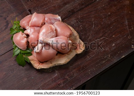 Raw chicken cuts or parts  like breast fillet,chicken stripes; chicken legs without skin arranged on a sliced wooden log base and garnished with curry leaves and placed on wooden background