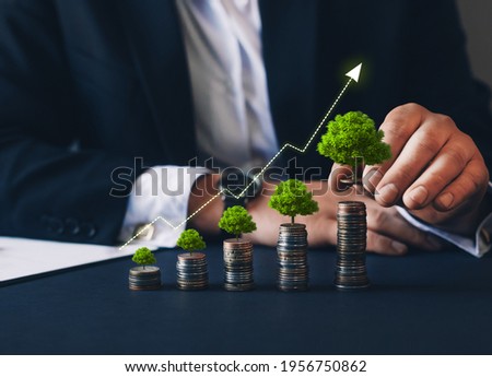 Businessman holding coin with graph and tree growing on money coin stack. Finance sustainable development. Green business growth.