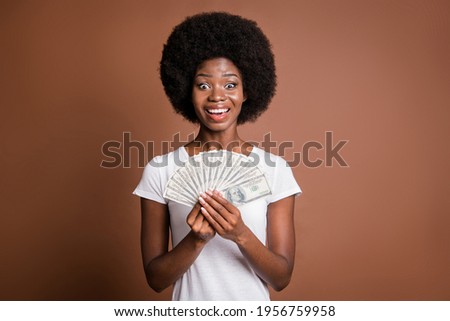 Photo portrait of woman showing money cash dollar banknotes smiling overjoyed rich isolated on brown color background