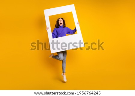 Full length body size view of attractive cheerful girl jumping holding big paper frame having fun isolated over bright yellow color background