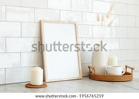 Blank picture frame mockup and home decor on table. White tiles bricks on background. Minimal Scandinavian style interior