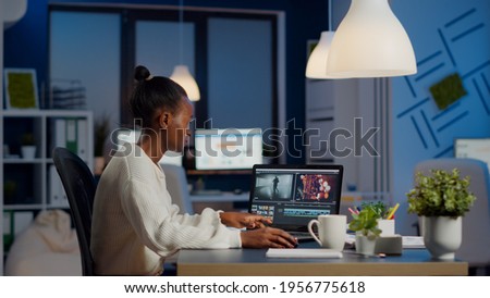 Black video editor working overtime at new project editing audio film montage sitting in start-up business office. Woman content creator using professional laptop, modern technology, network wireless