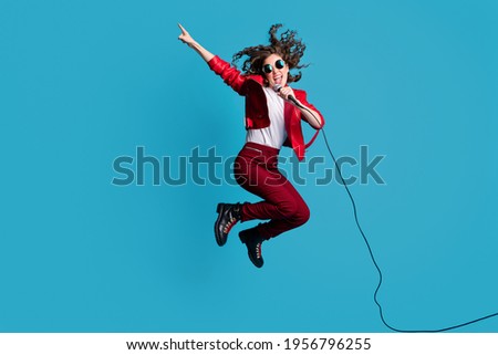 Full length portrait of crazy young girl jump sing direct finger empty space open mouth isolated on blue color background Royalty-Free Stock Photo #1956796255