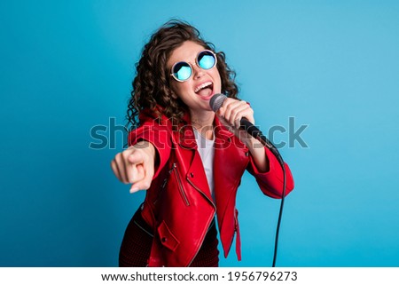 Photo of crazy carefree lady open mouth sing hold mic direct finger on you wear round sunglass isolated on blue color background Royalty-Free Stock Photo #1956796273