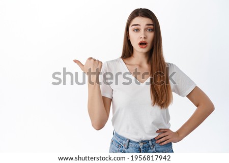 Surprised and curious girl pointing left aside at something interesting, asking question about product, asking question, interested with banner logo, standing over white background