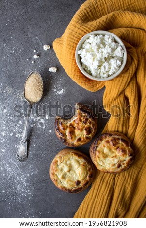 Sweet breakfast on a table. Top view photo of sweet round scones, cottage cheese in ceramic bowl, silver spoon, brown sugar, flour and yellow fabric. Gray background with copy space. 