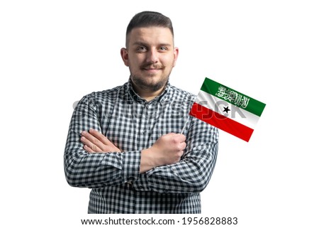 White guy holding a flag of Somaliland smiling confident with crossed arms isolated on a white background.