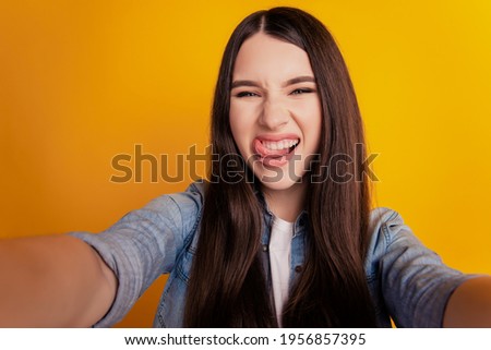 Close-up of young crazy funky woman taking selfie stick-out tongue on yellow background