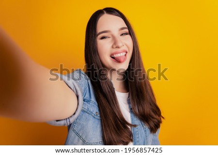 Close-up of young beautiful woman shoot selfie show tongue on yellow wall